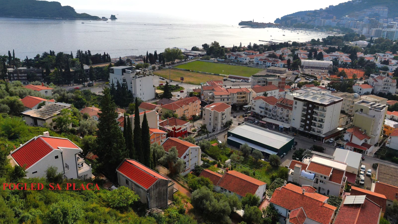 Panoramic view of Budva city and the sea from a land plot in Montenegro, featuring red-roofed buildings and the coastline.