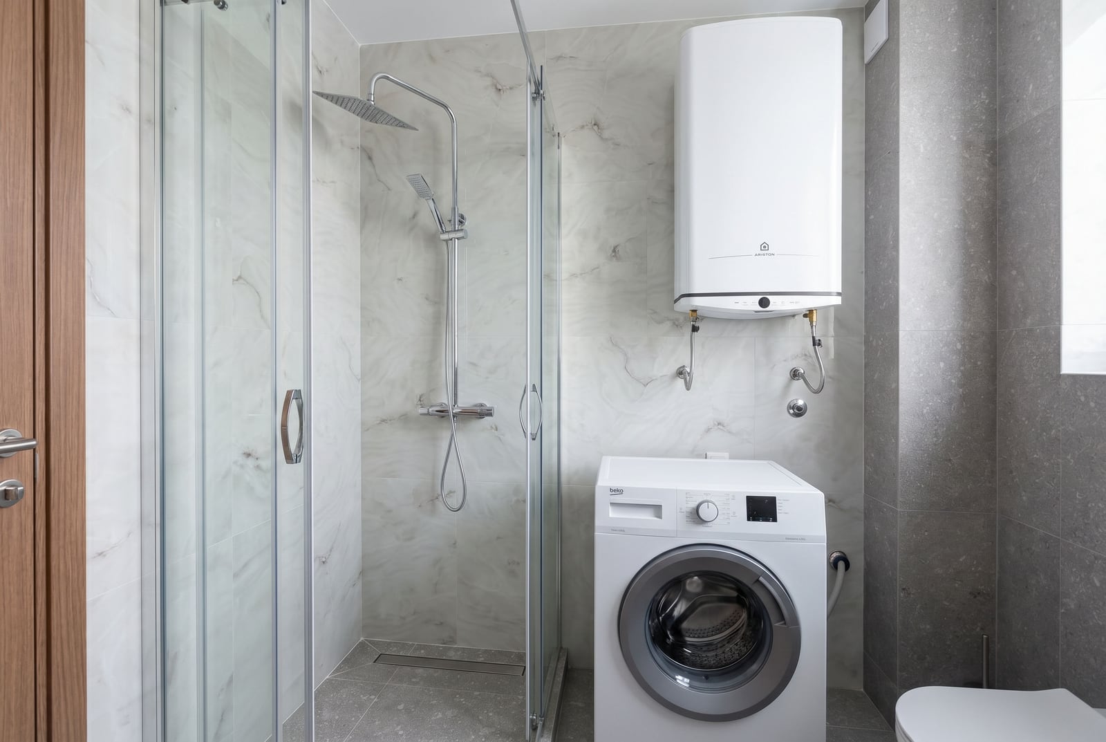 Modern bathroom in a Budva apartment, Montenegro: shower cabin, washing machine, and Ariston water heater.