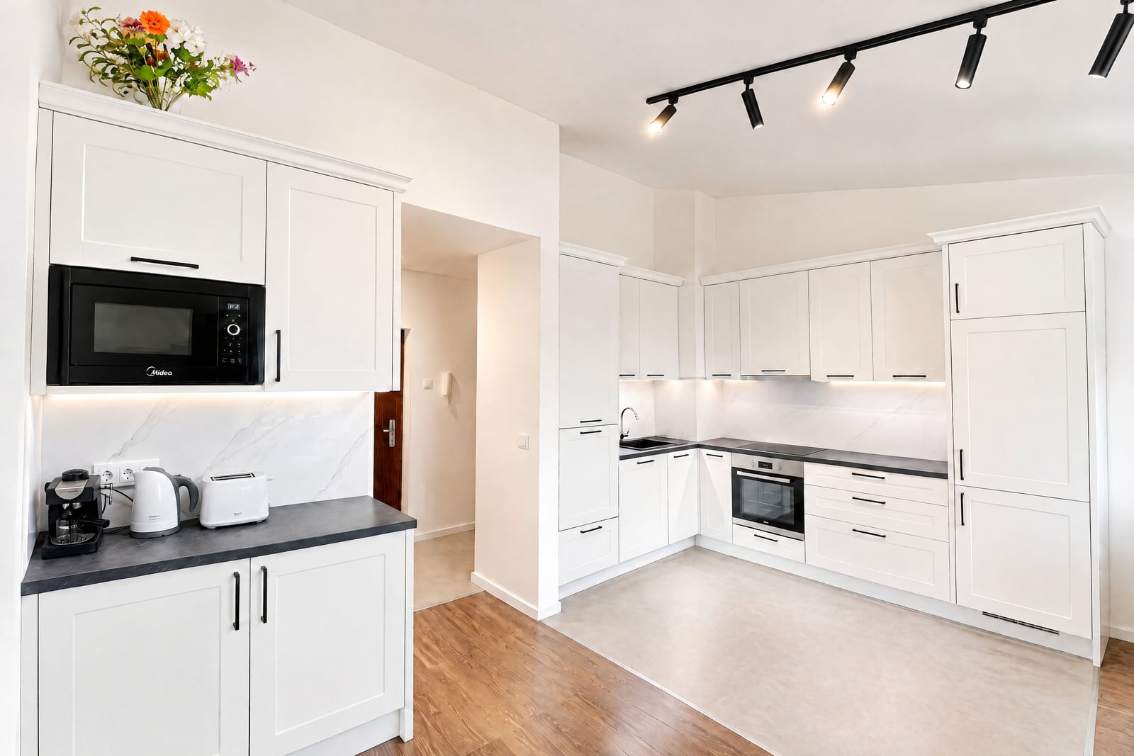 Modern kitchen with white cabinets, black countertops, microwave, oven, and small appliances like a toaster.
