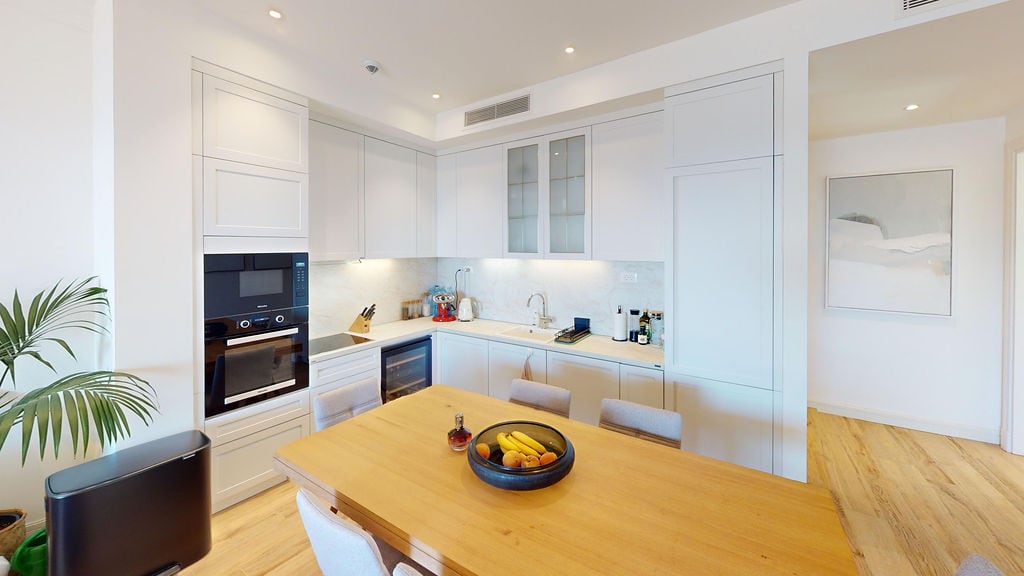 Modern kitchen in an apartment, Luštica, Montenegro: light-colored kitchen set, built-in appliances, and a wooden dining table.