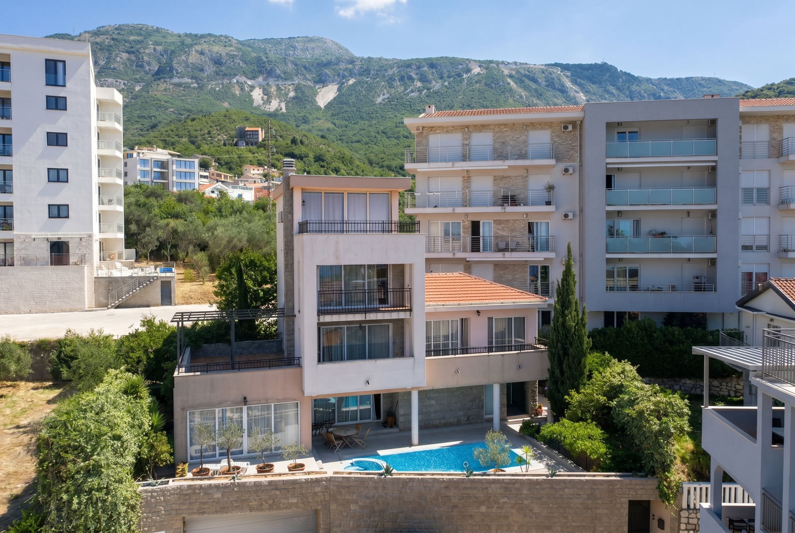 Modern villa with a swimming pool and terrace in Becici, Montenegro, set against a backdrop of picturesque mountain landscapes.