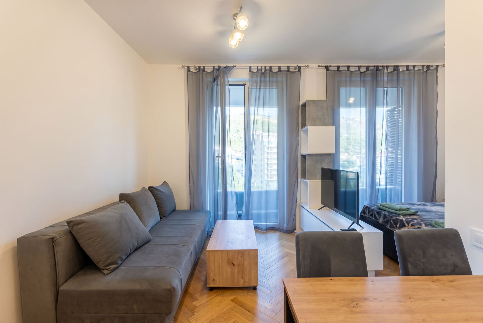 Living room with a grey sofa and balcony access in an apartment in Bečići, Montenegro: modern interior with parquet flooring.