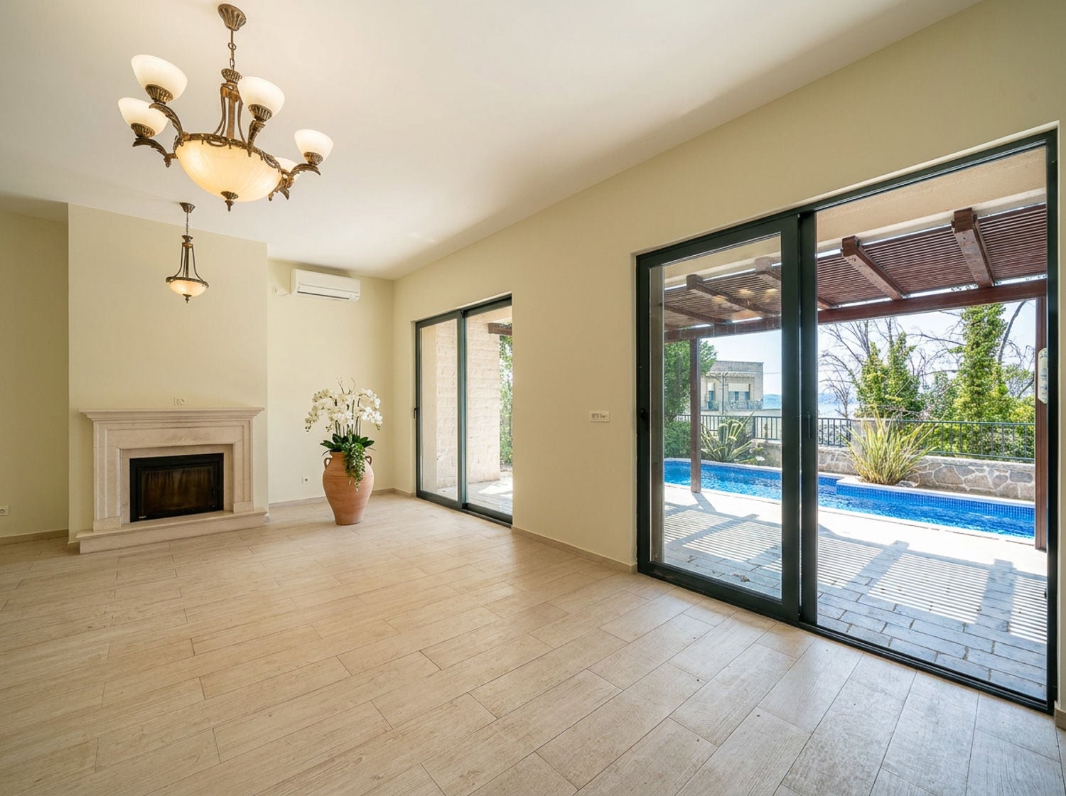 Empty room with fireplace, chandelier, and sliding doors leading to a pool terrace.