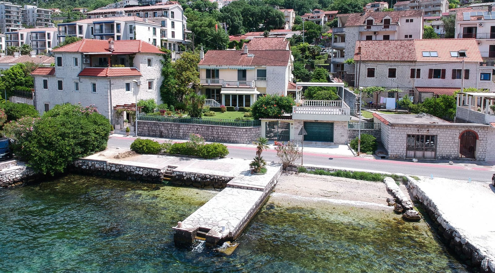 Villa in Dobrota, Montenegro: view of the house with a terrace, private pier, and sea access surrounded by greenery.