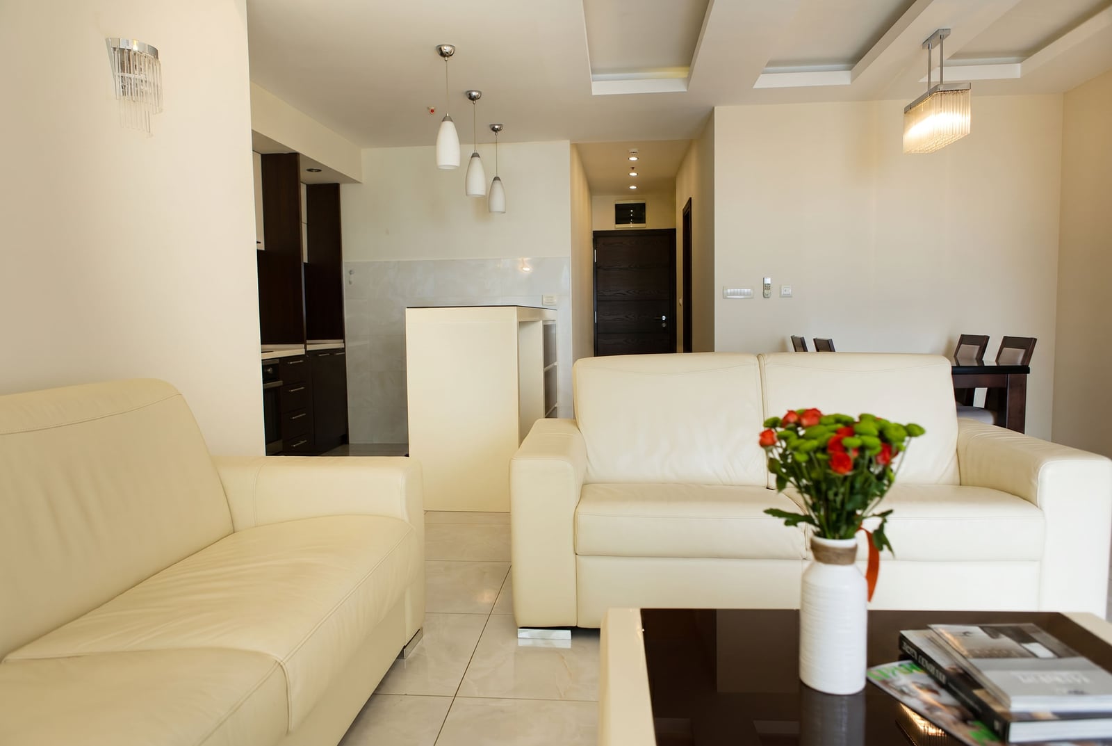 Living room with white leather sofas and a kitchen in an apartment in Becici, Montenegro. Modern interior with a dining area.