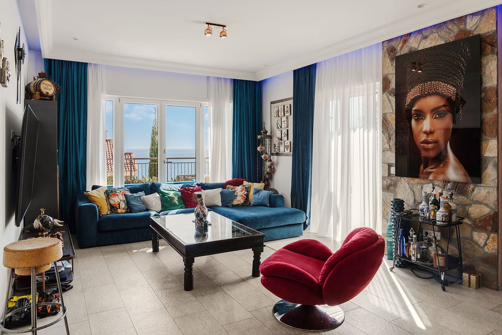 Living room in a Luštica townhouse, Montenegro: blue sofa, red armchair, stone finishes, and panoramic sea view.
