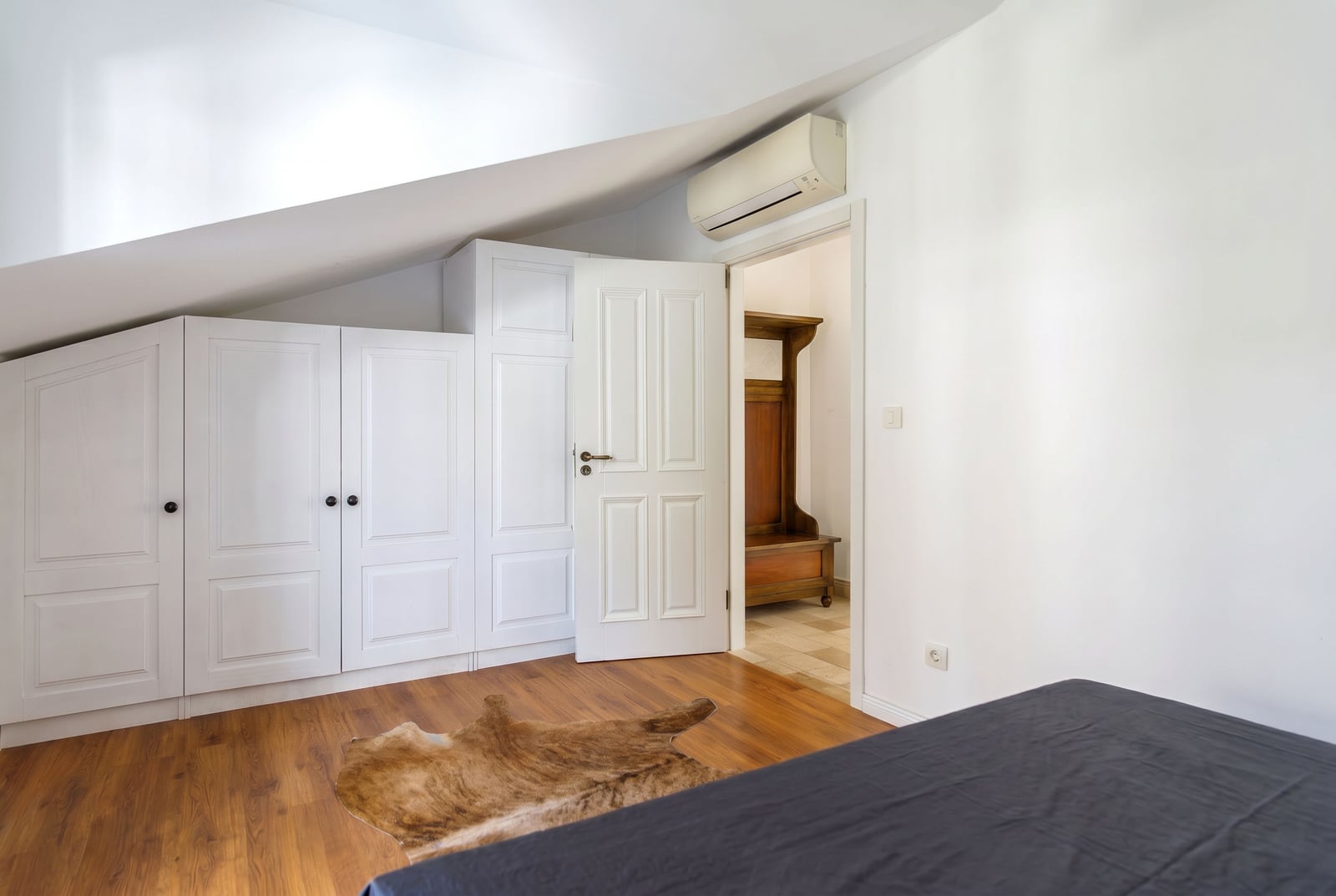 Bedroom in a penthouse in Risan, Montenegro: built-in white wardrobe, mansard ceiling, laminate flooring, and a fur rug.