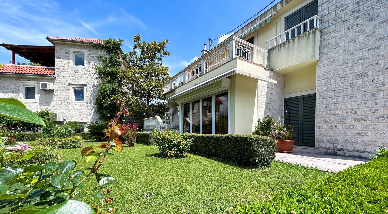Two-story stone villa with a terrace and a well-kept garden in Dobrota, Montenegro: exterior of the house with a green lawn.