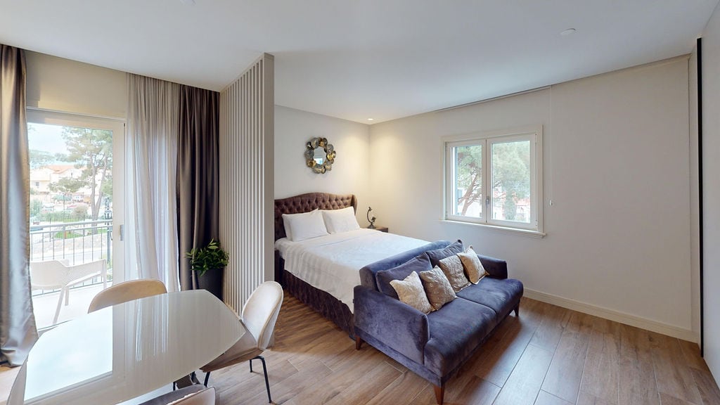 Modern bedroom with a double bed, sofa, and balcony access in the Luštica apartments, Montenegro.