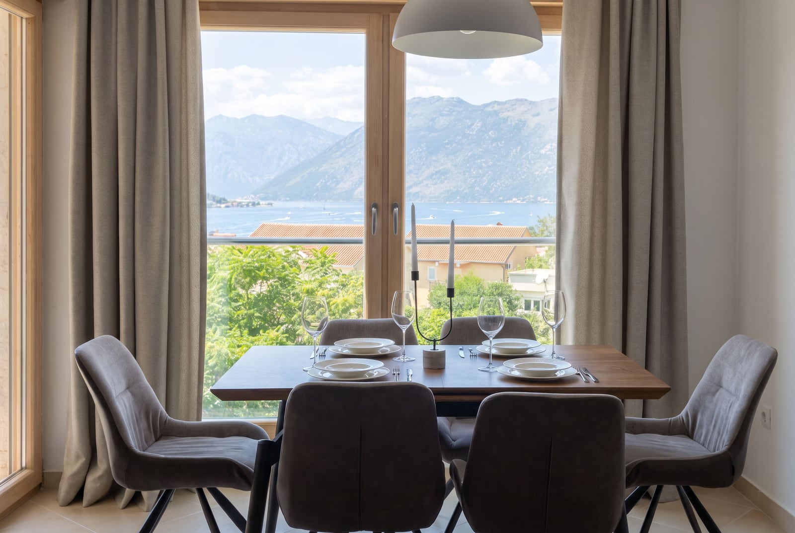 Dining area in an apartment in Dobrota, Montenegro: a table with a view of the Bay of Kotor and the mountains through a panoramic window.