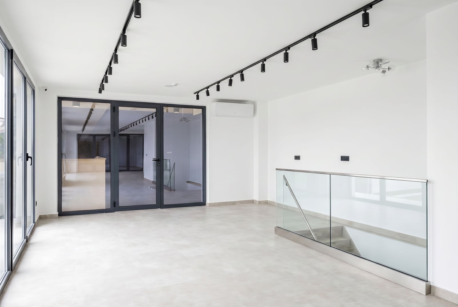 Modern office in Budva, Montenegro: bright space with panoramic windows, track lighting, and a glass staircase