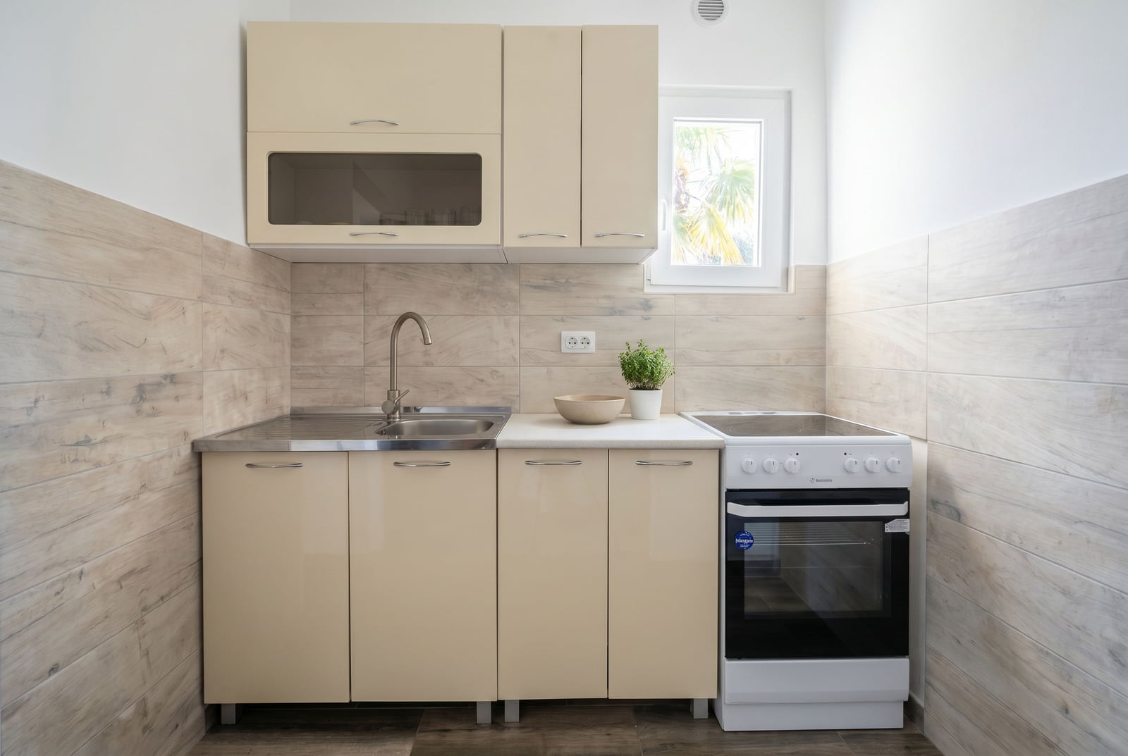 Compact kitchen in a house, Krašići, Montenegro: beige cabinetry, stove, sink, and wood-look tile finish.