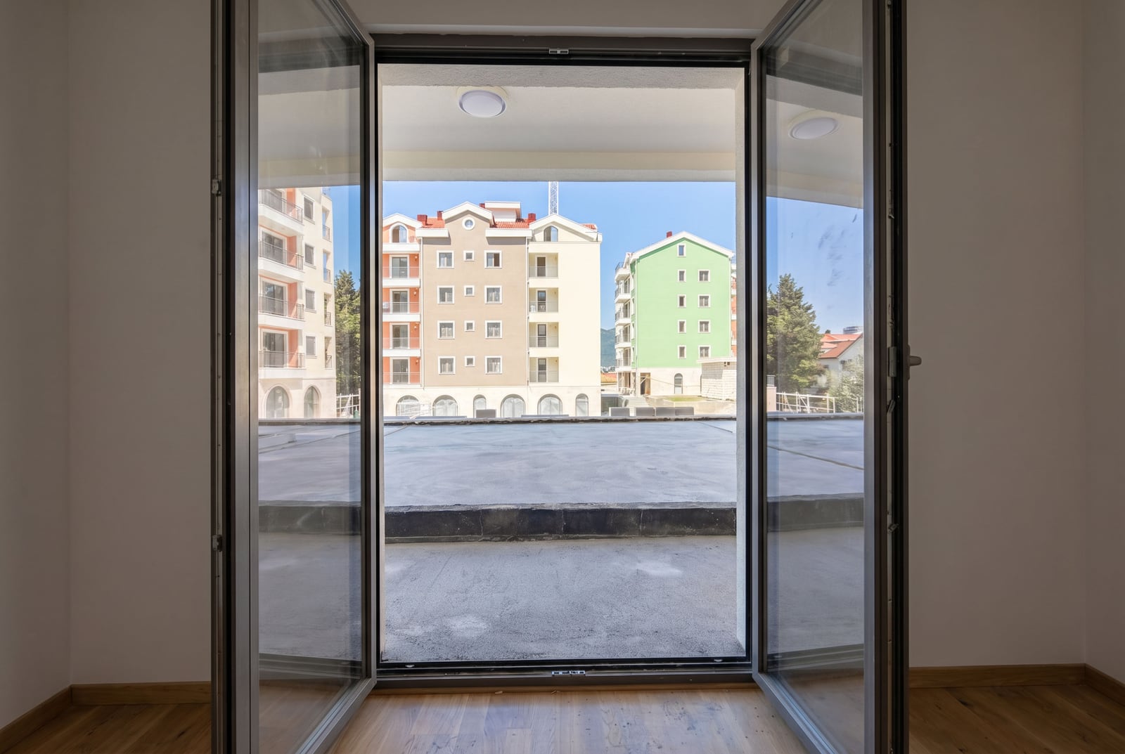 View from the panoramic doors of an apartment in Tivat, Montenegro, overlooking a spacious open terrace and the residential complex.