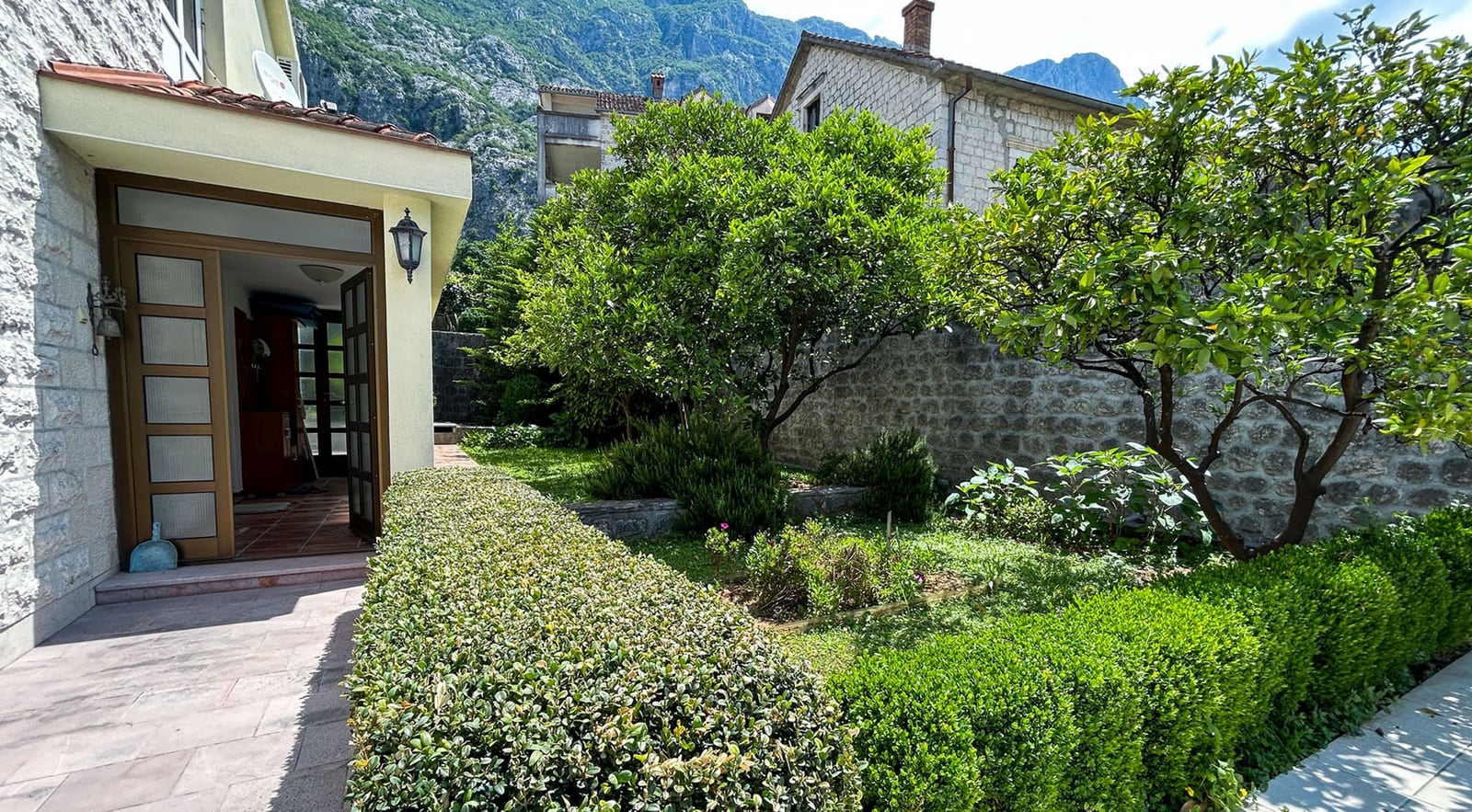 Cozy green garden and terrace of a stone villa in Dobrota, Montenegro, with mountain views and landscape design.