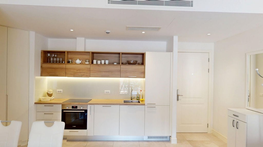 Modern kitchen with built-in appliances in an apartment, Luštica, Montenegro: white facades, wooden shelves, and lighting.