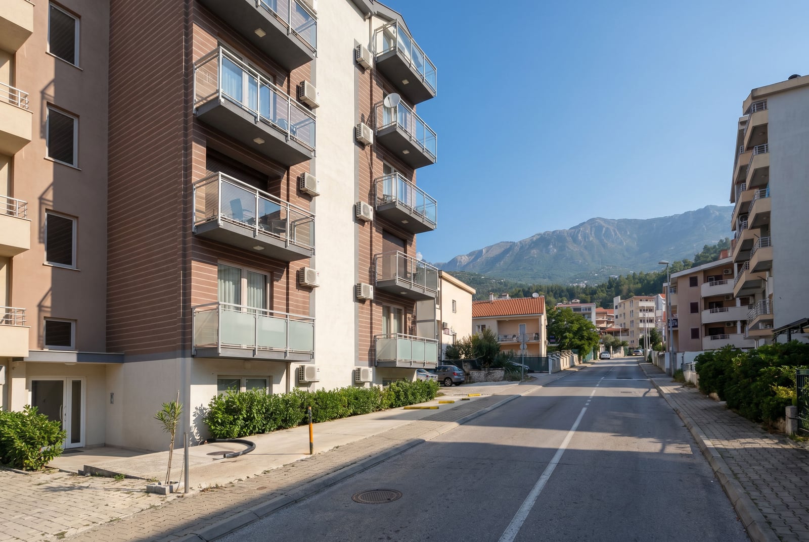 Modern residential building with balconies in Budva, Montenegro, street view and mountain landscape on a sunny day.