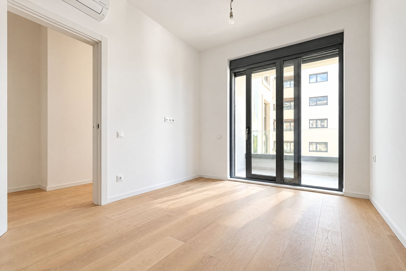 Empty room with light wood flooring, white walls, and a large glass door leading to a balcony.