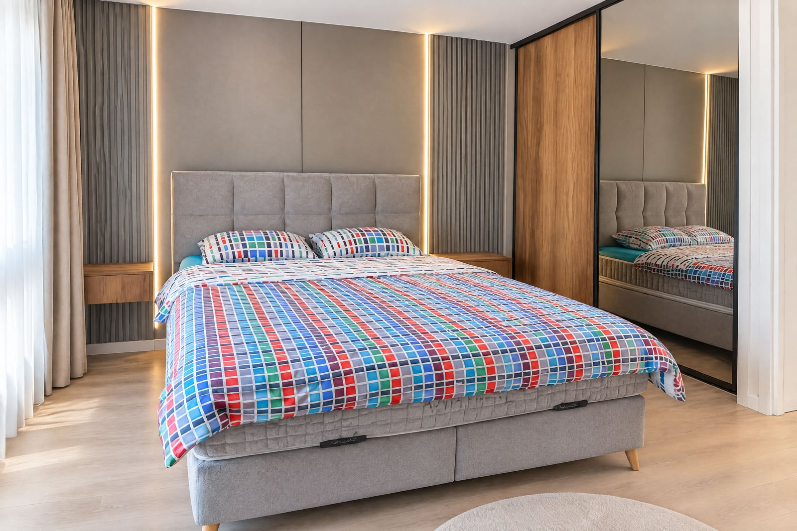 Modern bedroom featuring a large grey bed with colorful checkered bedding and a wooden wardrobe unit.