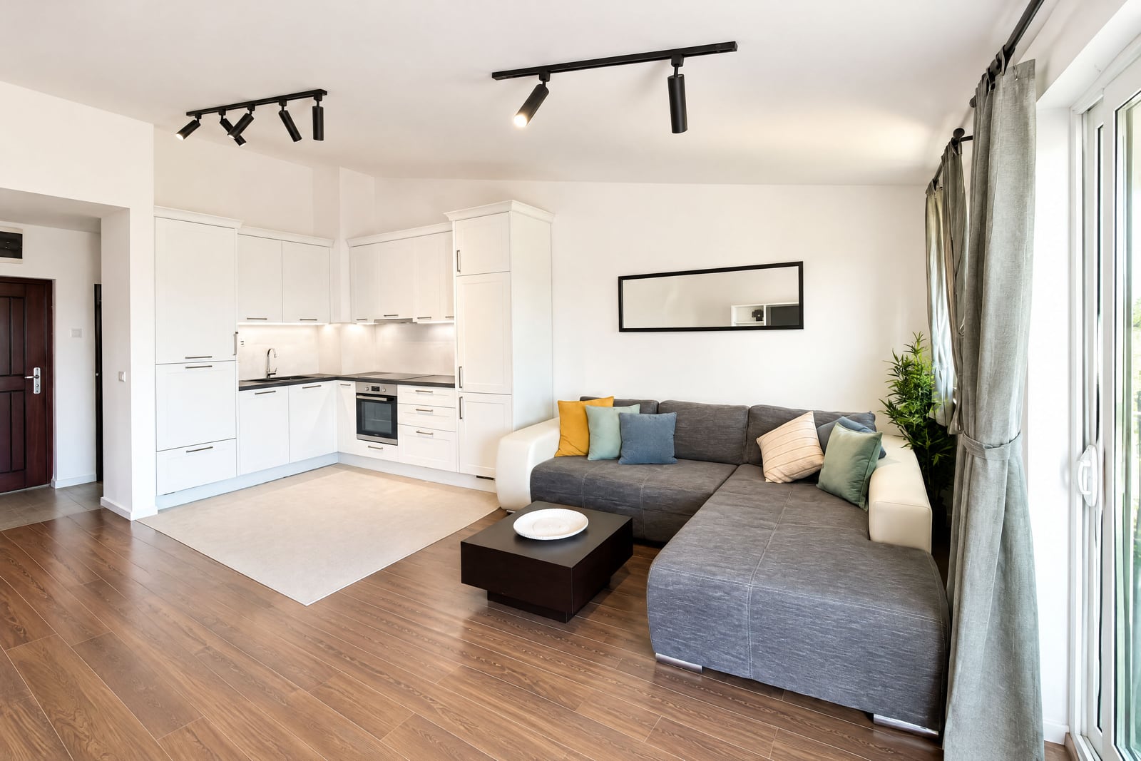 Modern living room with a grey sofa and open white kitchen in the background.