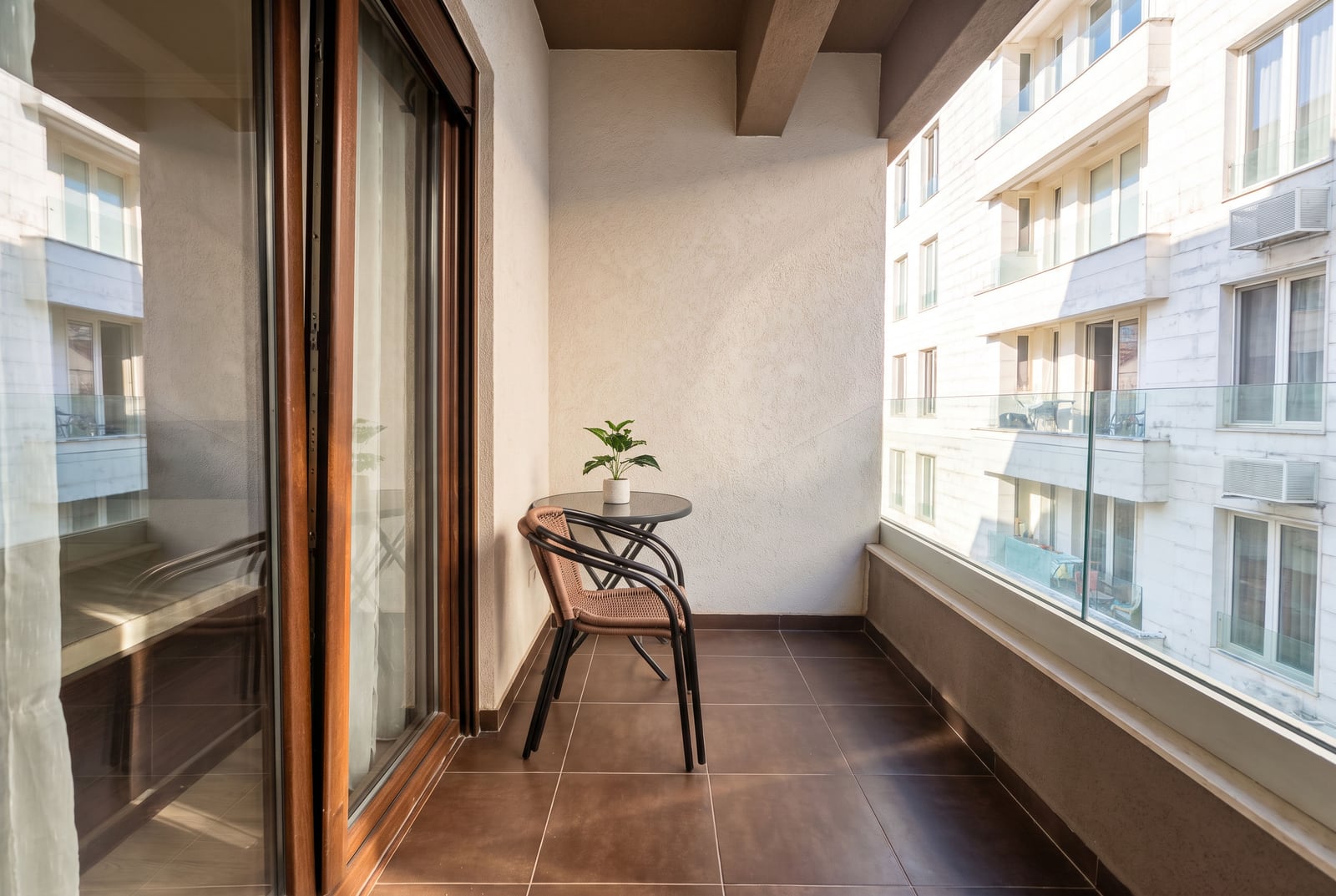 Spacious balcony with tile flooring, wicker chairs, a table, and glass railing in an apartment in Budva, Montenegro.