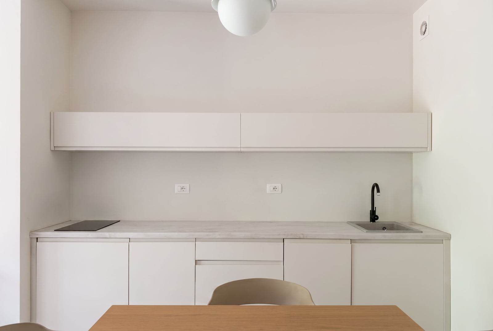 Modern white kitchen in an apartment in Bečići, Montenegro: built-in appliances, stone countertop, and black faucet.