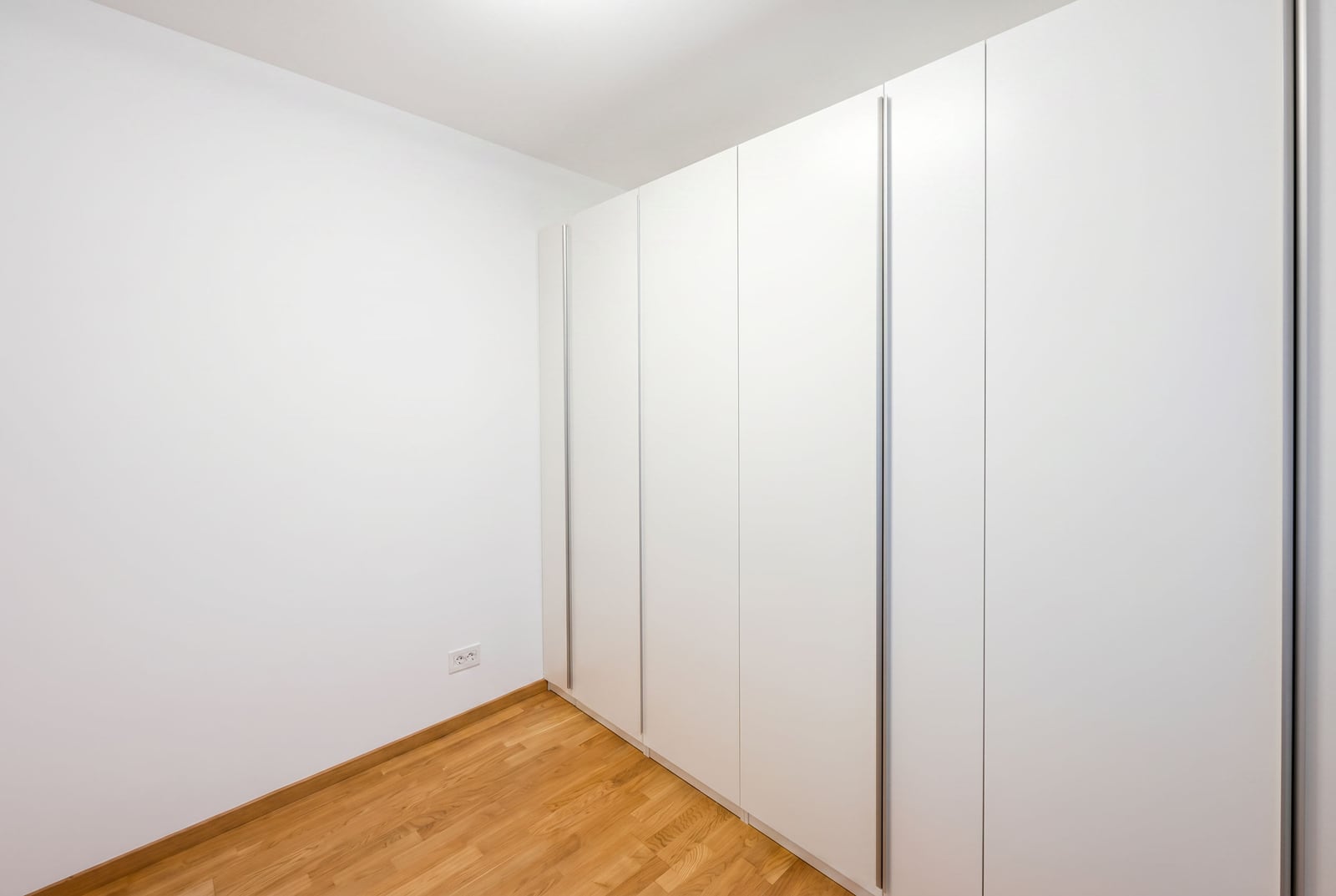 Built-in white wardrobe in the bedroom of a modern apartment in Bečići, Montenegro, with light wood accents.