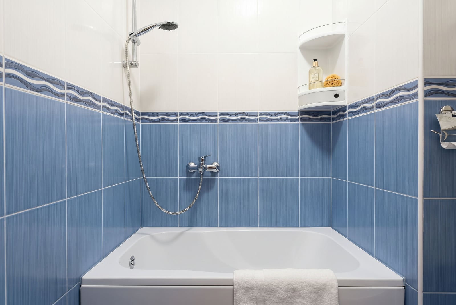 Bathroom in an apartment in Bar, Montenegro: white bathtub, blue tiles, and chrome shower in the interior.