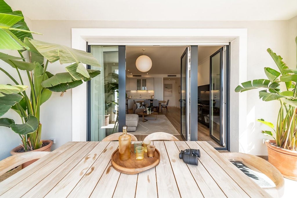 Terrace with a wooden table and plants in the apartment of the Luštica residential complex, Montenegro, view of a modern living room with kitchen.
