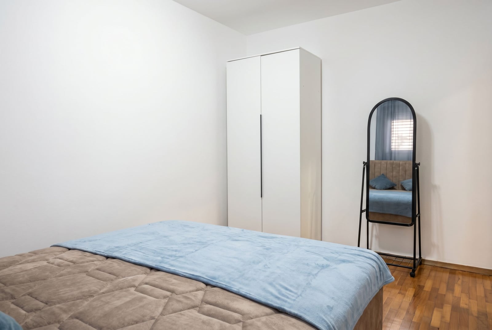 Bedroom in an apartment in Budva, Montenegro: a double bed, a white wardrobe, and a floor mirror in a modern interior.