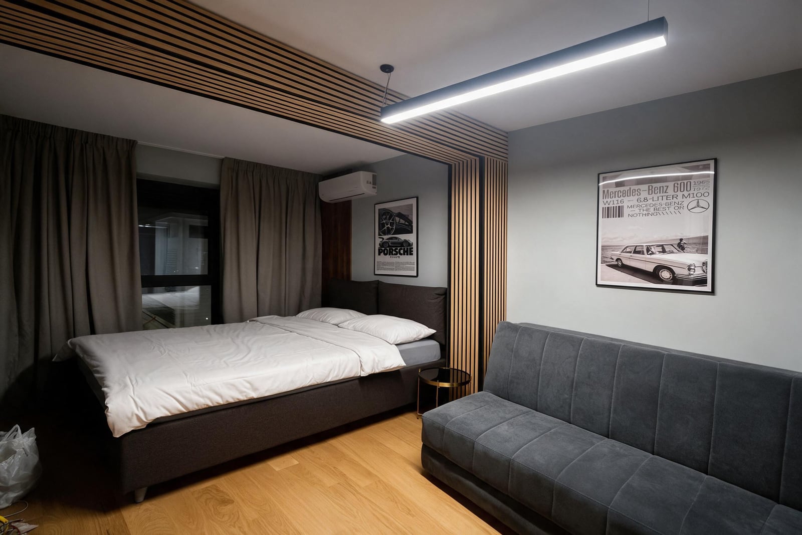 Modern bedroom featuring a double bed, grey sofa, and automotive posters on the wall.
