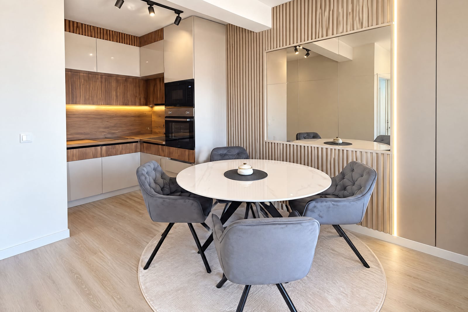 Modern kitchen with wood cabinets, built-in appliances, and a round white dining table surrounded by grey chairs.