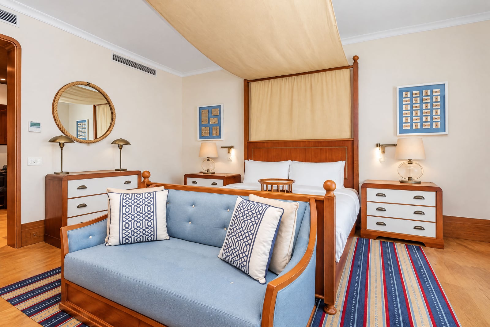 Bedroom featuring a canopy bed, blue sofa, striped rug, and wooden furniture with white drawers.