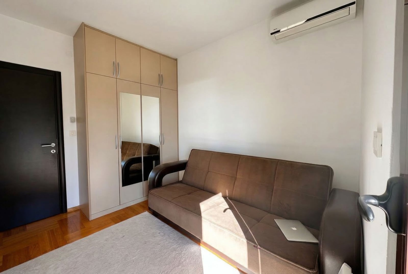Living room in an apartment in Budva, Montenegro: brown sofa, built-in mirrored wardrobe, and air conditioner in the interior.