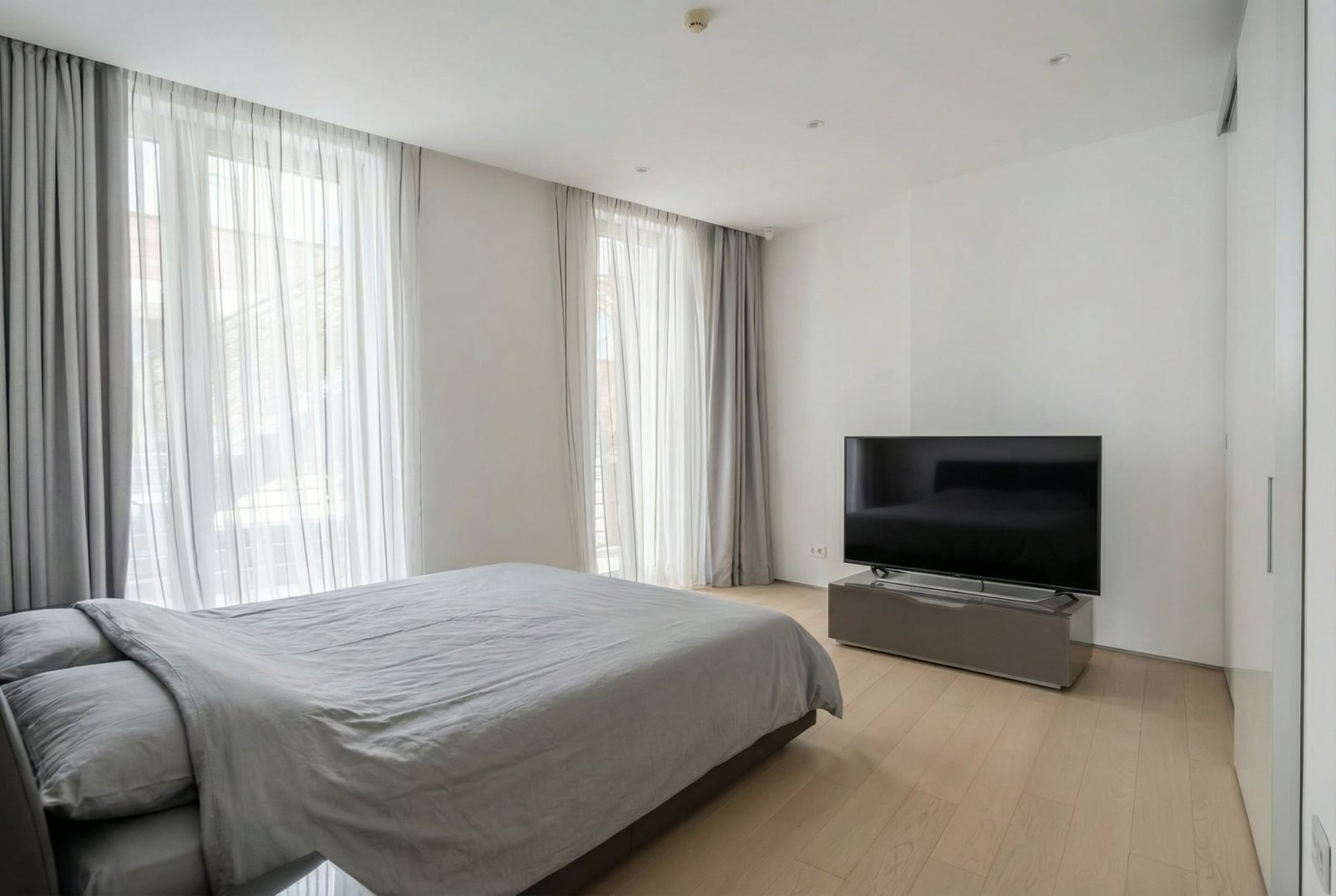 Modern bedroom in Dukley complex, Budva, Montenegro: double bed, TV, panoramic windows with light curtains.