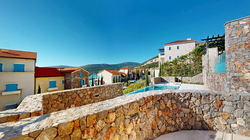 View of a residential complex in Luštica, Montenegro: stone facade finishes, an outdoor swimming pool, and a mountain panorama.