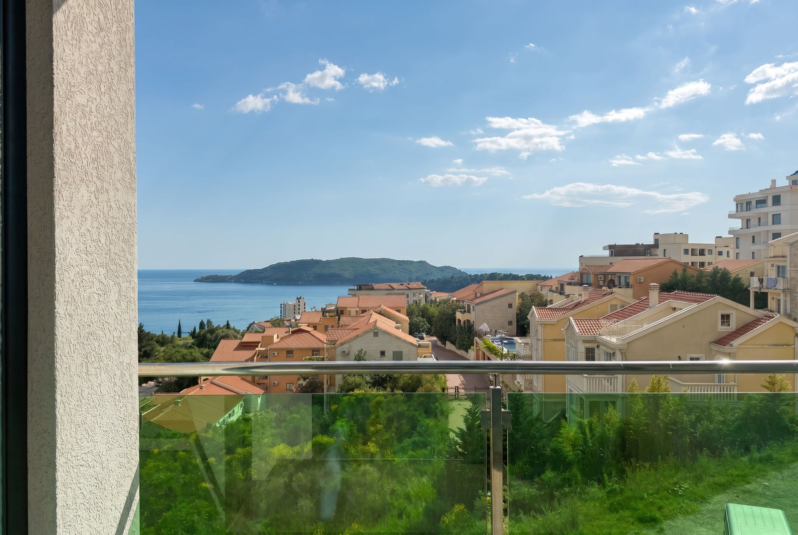 View from the apartment balcony in Bečići, Montenegro: panoramic view of the sea, the island of Sveti Nikola, and the tiled roofs of villas.