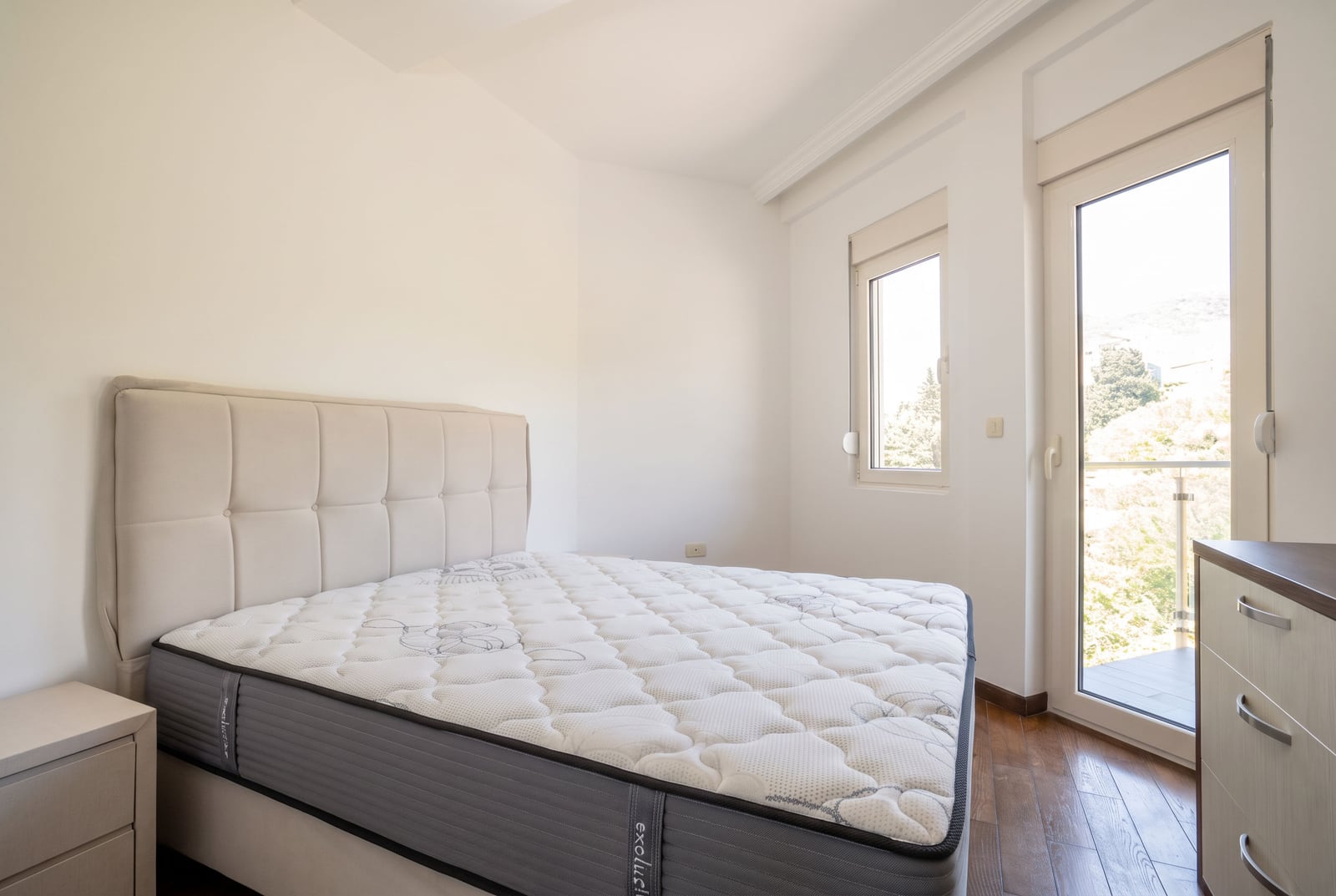 Bright bedroom featuring a double bed with upholstered headboard and wooden flooring.