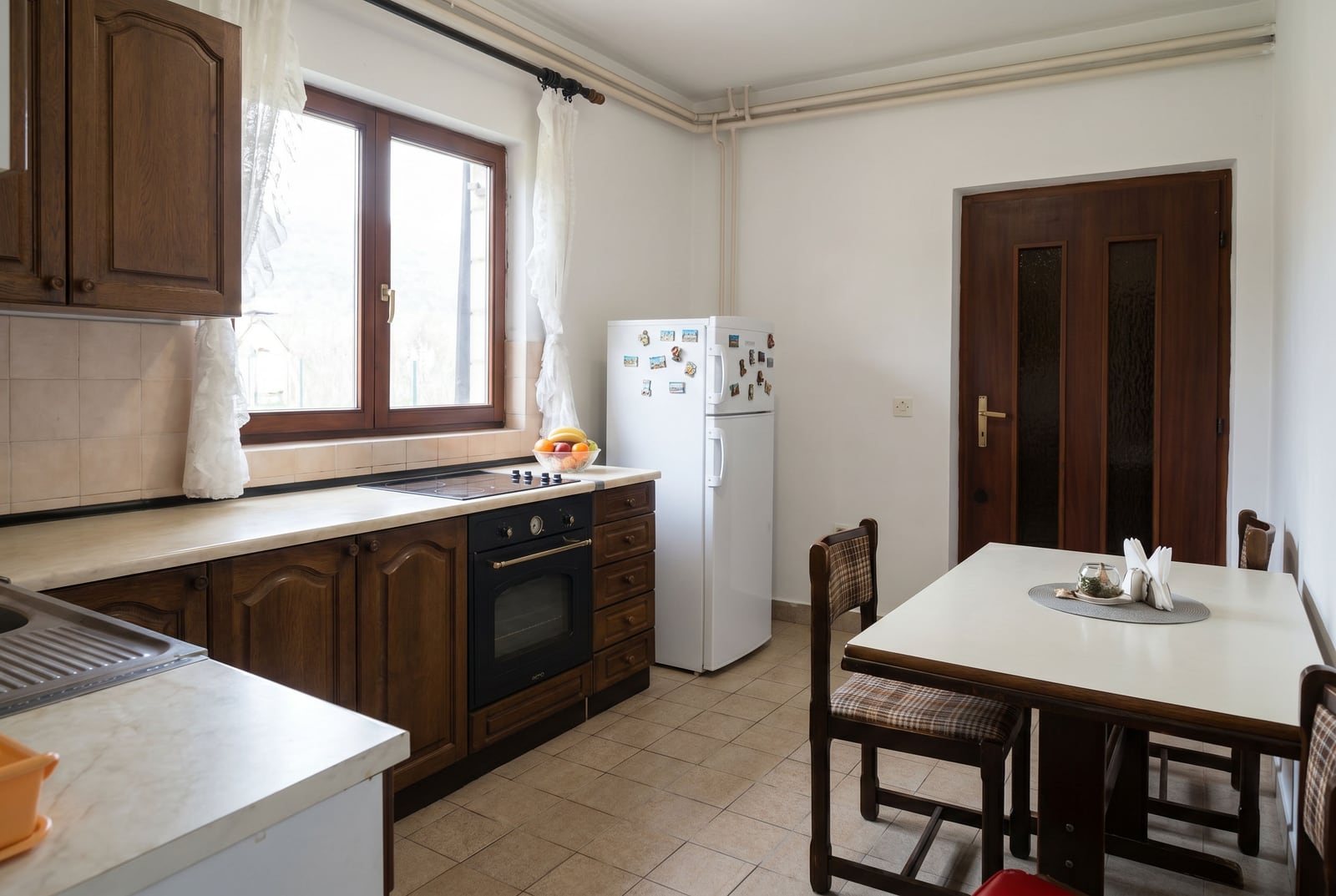 Kitchen with wooden cabinetry and a dining area in a house, Lastva, Montenegro. Bright room with household appliances.