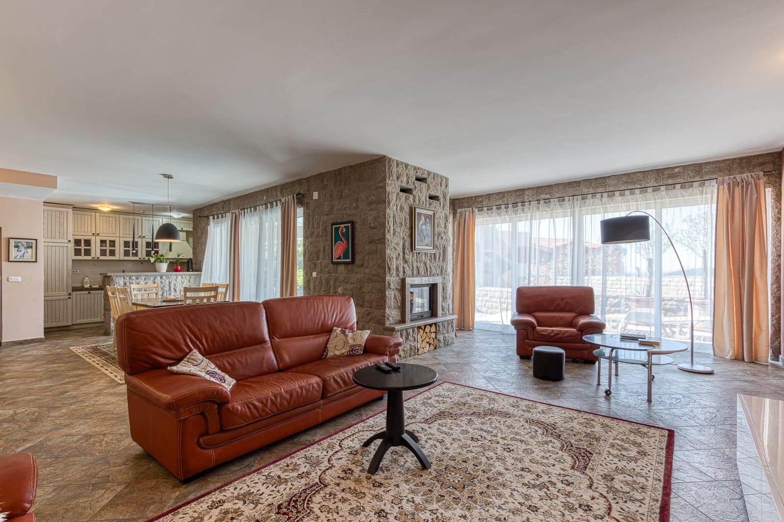 Living room with a stone fireplace and leather furniture in a villa in Bečići, Montenegro. Open-plan layout with a kitchen and terrace.