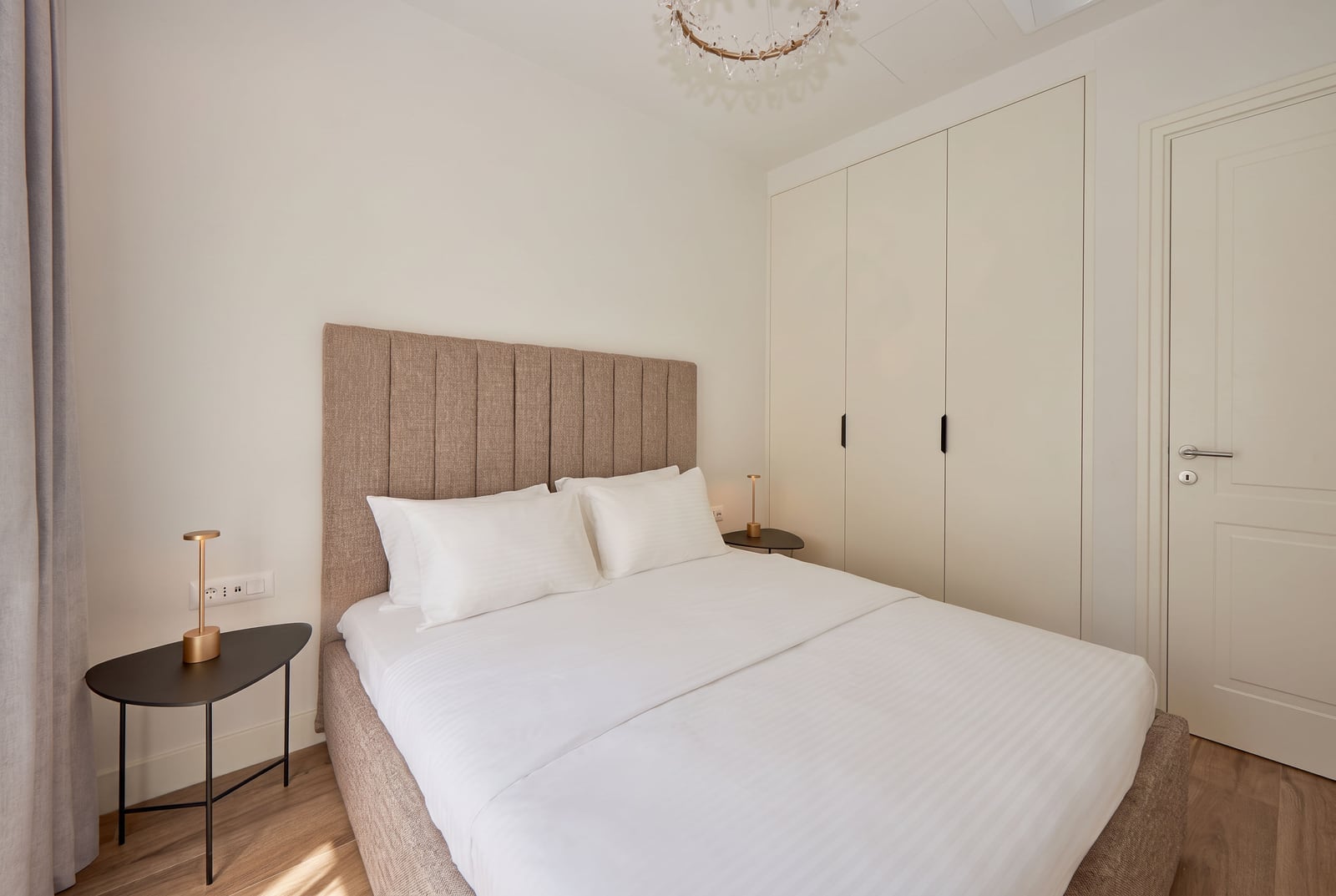 Modern bedroom featuring a double bed with upholstered headboard, white linens, nightstands with lamps, and built-in wardrobes.