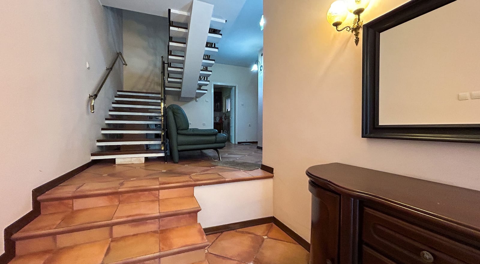 Villa interior in Dobrota, Montenegro: an entryway with a staircase, tiled floor, a dresser, and an armchair in the living room.