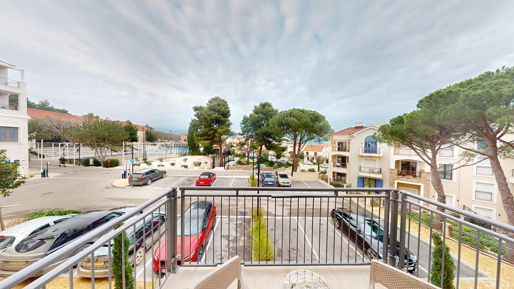 View from the balcony of an apartment in Luštica, Montenegro: parking, residential complex, and pine trees against a cloudy sky.