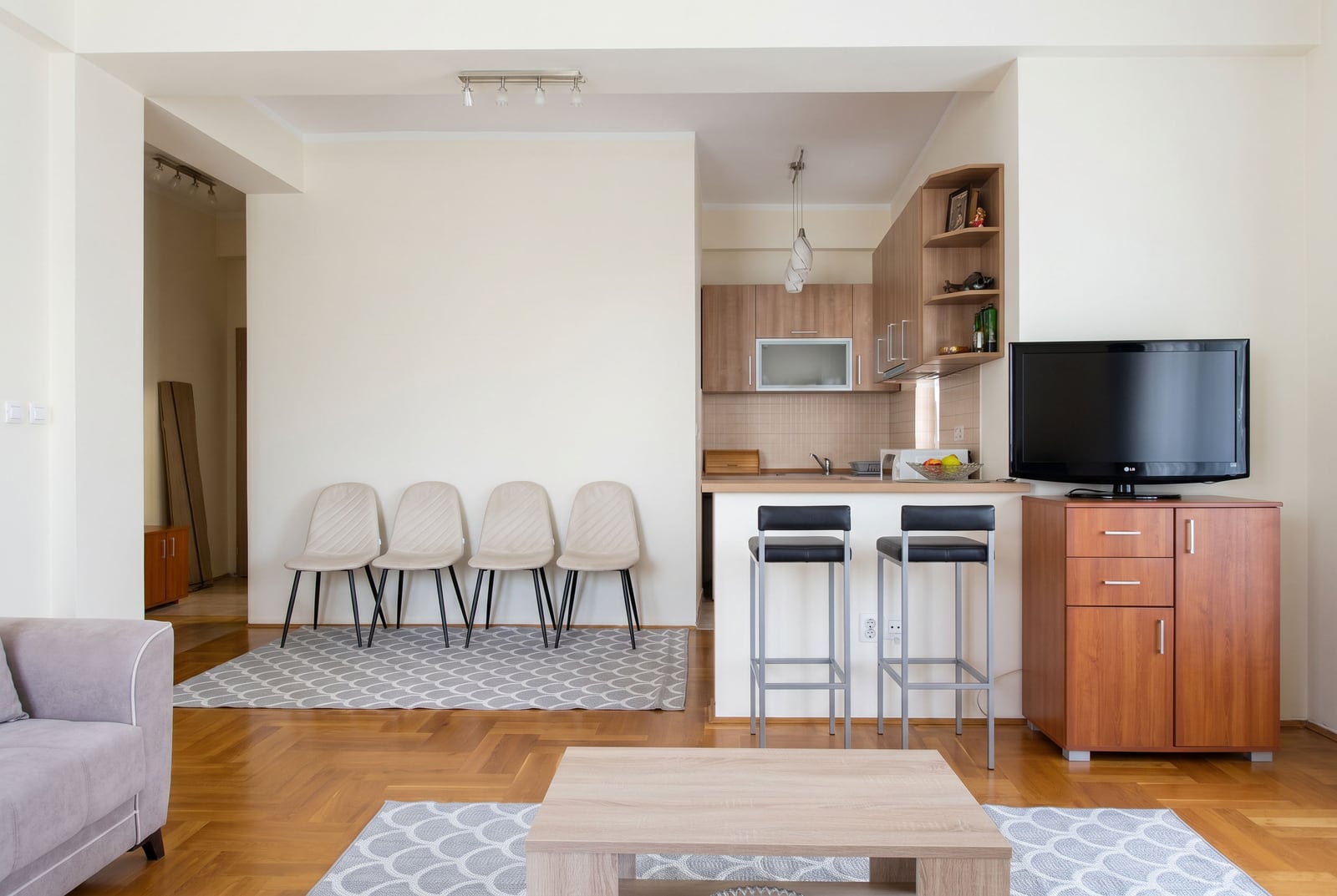 Living room with kitchen in an apartment in Budva, Montenegro: light-colored furniture, breakfast bar, parquet flooring, and modern finishes.