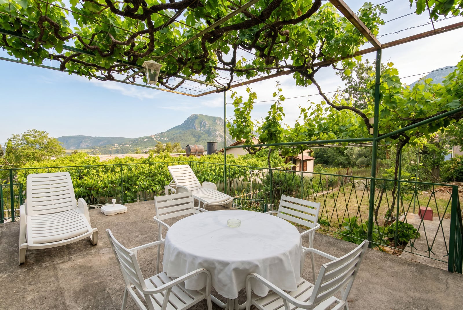 Terrace with a grape pergola, sun loungers, and mountain views at a house in Sutomore, Montenegro.