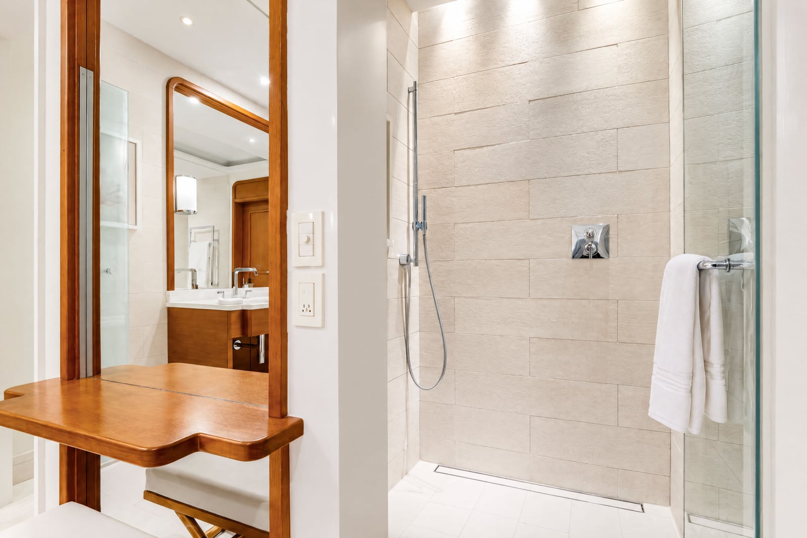 Bathroom featuring a tiled shower stall, wooden vanity table, and large mirror.
