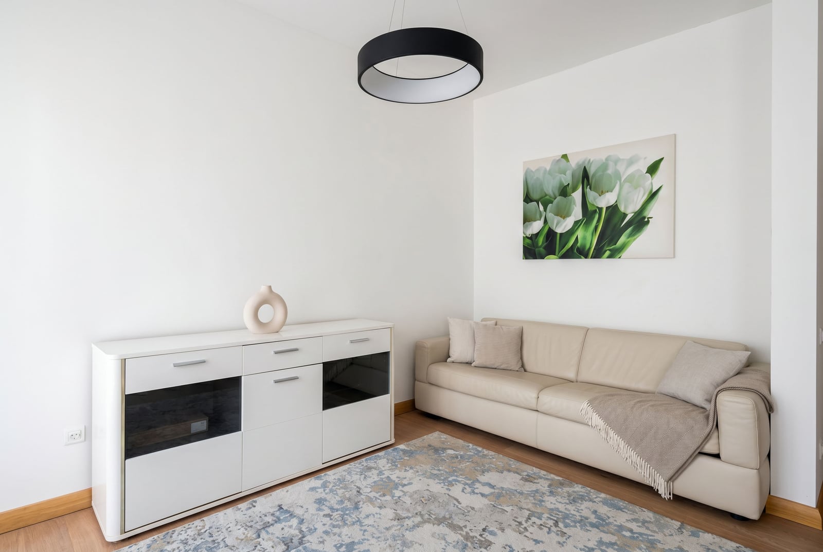 Bright living room in a Budva apartment, Montenegro: beige leather sofa, modern white media console, and wall decor.