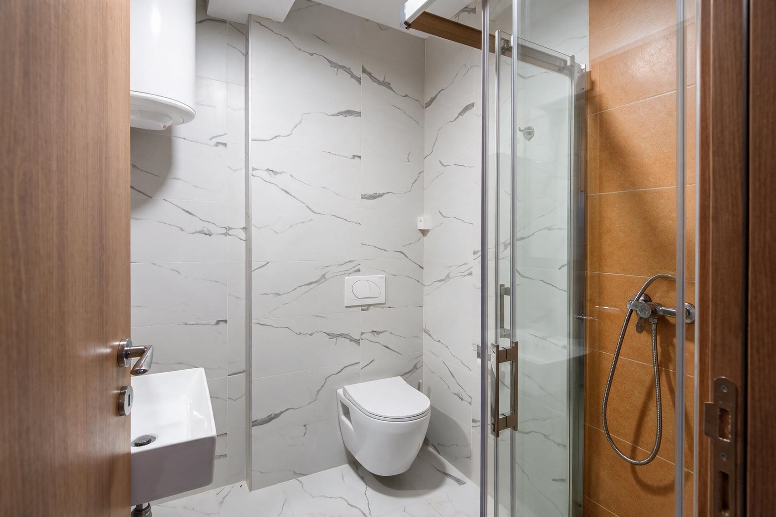Modern bathroom with a shower cabin, white sanitary ware, and marble tiles in an apartment in Budva, Montenegro.