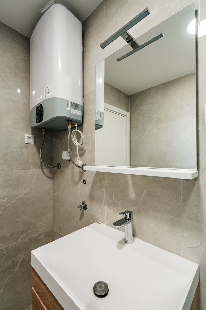 Modern bathroom in Budva residential complex, Montenegro: white sink, backlit mirror, and wall-mounted boiler.