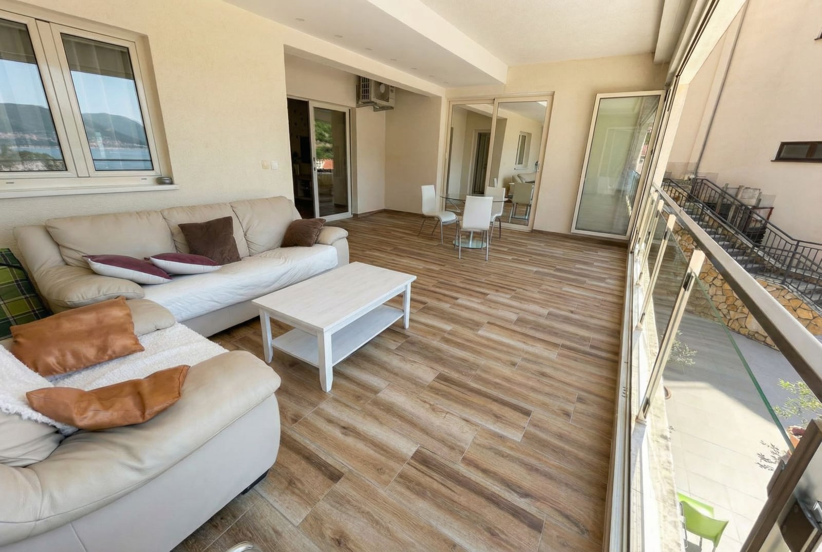 Spacious terrace with sea view in an apartment, Pržno, Montenegro: light furniture, panoramic glazing, and tile.