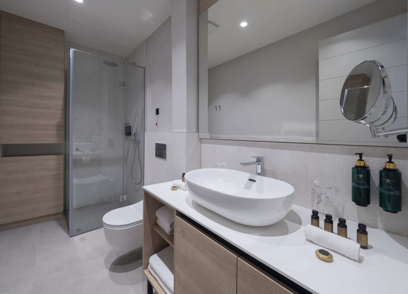 Modern bathroom featuring a glass shower enclosure, wall-mounted toilet, and vessel sink on a wooden vanity with toiletries.
